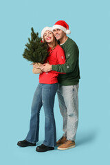 Poster - Happy young couple in Santa hats with Christmas tree on blue background