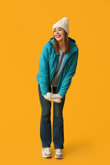 Sticker - Beautiful young happy woman in warm winter clothes on yellow background