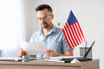 Handsome young man with documents and flag of USA working at table in office