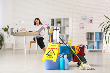 Sticker - Businesswoman working in office with janitor's trolley, cleaning supplies and caution sign on floor