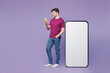 © ViDi Studio - Full body young happy man he wear violet t-shirt casual clothes big huge blank screen mobile cell phone with workspace copy space mockup area use smartphone isolated on plain light purple background.