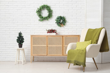 Wall Mural - Interior of living room with armchair, chest of drawers and Christmas decor near white brick wall