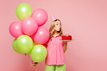 Poster - Young surprised shocked woman wear shirt cone hat celebrate birthday holiday and hold bunch of colorful air balloons, cake blow out candles isolated on plain pastel pink background. Lifestyle concept.