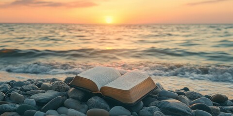 Poster - Bible placed on small stones in front of the green sea under an orange sky. Copy space.