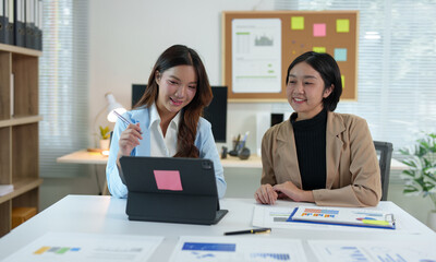 two young businesswomen pointing to plans, statistics, and data graphs and explaining the conditions