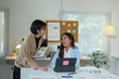 © crizzystudio - Two Asian businesswomen use laptops and smartphones in an open space office. Business concept. Data analysis, roadmap, marketing, accounting, auditing.