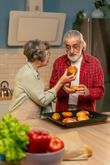 in bright kitchen an elderly woman in a light green shirt is happy about the prepared pies her husband is happy tasting pastries