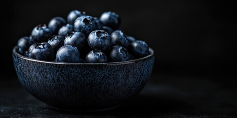 Poster - Fresh, juicy blueberries in a bowl against a black background. Low key photography.