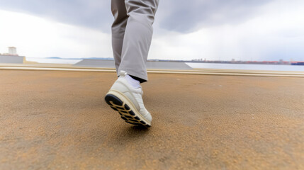 Low-angle shot of a person in casual sneakers walking on a pavement, highlighting footwear and movement against an overcast sky