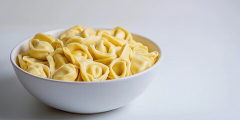 Aufkleber - Fagottini tortellini pasta in a white bowl set against a white background, softly lit, studio shot, angled view, copy space.