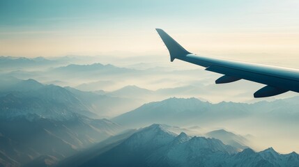Poster - Airplane wing is flying over a mountain range covered with snow. The sun is rising, creating a warm, hazy glow over the landscape