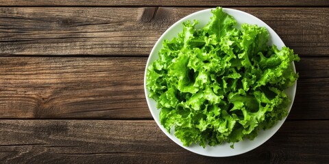 Wall Mural - Fresh lettuce leaves in a white plate on a wooden table background. Top view. Copy space.