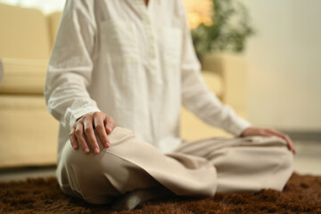 Peaceful young woman sitting in lotus pose on floor meditating at home