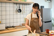 © Prathankarnpap - Attractive young woman cooking on kitchen counter while talking on cellphone