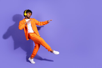 Wall Mural - Full length photo of handsome good mood guy wear orange suit listen music earphones dancing emtpy space isolated violet color background