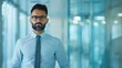 © Vilaysack - Confident businessman in a modern office hallway, wearing glasses and a formal shirt. Professional environment with glass walls.