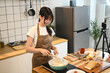© Prathankarnpap - Young woman blogger cooking and recording video with her mobile phone in the kitchen
