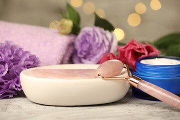 Canvas Print - Face roller, gua sha tool, cosmetic product and beautiful flowers on gray textured table against blurred lights, closeup