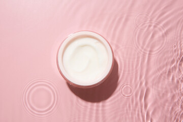 Sticker - Cosmetic product. Jar with cream in water on pink background, top view