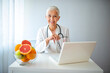 © Dragana Gordic - Senior Doctor Smiling at Desk with Laptop and Fresh Fruits