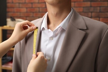 Wall Mural - Professional tailor measuring jacket lapel on client in atelier, closeup