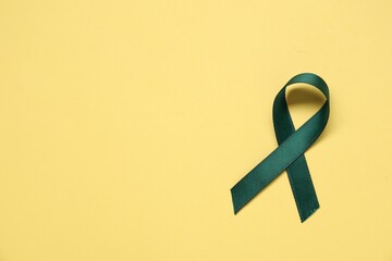 Canvas Print - Green awareness ribbon on yellow background, top view. Space for text