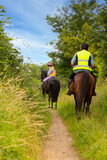 Two horseback riders and their horses enjoying riding in the English countryside, along bridleways and narrow tracks.Both riders are wearing reflective gear to be seen and be safe.