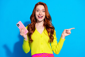 Wall Mural - Photo portrait of pretty young girl hold gadget excited point empty space wear trendy yellow outfit isolated on blue color background