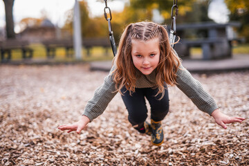 Little girl having fun on a playground in public park on autumn day.