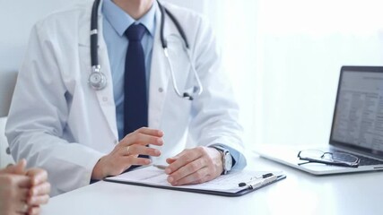 Wall Mural - Doctor and a patient. The physician, wearing a white medical coat over a blue shirt and tie, gesturing with his hands during a consultation in the clinic. Medicine concept