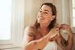 © Malambo/peopleimages.com - Woman, smile and brush hair in bathroom for morning routine, getting ready and haircare in home. Reflection, happy person and hairbrush for cosmetics grooming, beauty hairstyle or self care in mirror