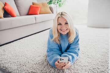 Wall Mural - Photo of pretty aged woman lying carpet floor use phone wear pullover free time modern apartment indoors