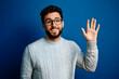 © john - Young handsome man with beard wearing casual sweater and glasses over blue background Waiving saying hello happy and smiling, friendly welcome gesture