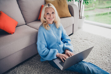 Wall Mural - Photo of pretty aged woman sit carpet floor use laptop wear pullover free time modern apartment indoors