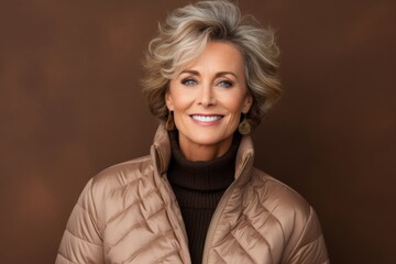 Poster - Portrait of a happy woman in her 50s sporting a quilted insulated jacket isolated on soft brown background