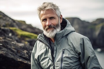 Wall Mural - Portrait of a content man in his 60s wearing a lightweight packable anorak over rocky cliff background