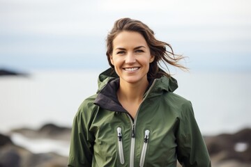 Wall Mural - Portrait of a smiling woman in her 30s wearing a windproof softshell while standing against serene seaside background