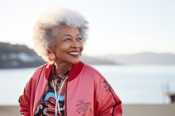 Sticker - Portrait of a tender afro-american woman in her 70s sporting a stylish varsity jacket while standing against serene seaside background