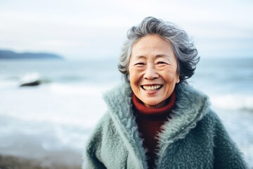 Canvas Print - Portrait of a cheerful asian elderly woman in her 90s wearing a cozy sweater over crashing waves background