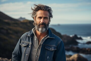 Sticker - Portrait of a content man in his 50s sporting a rugged denim jacket while standing against rocky shoreline background