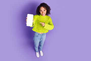 Wall Mural - Photo of american young funky girl in green sweater finger pointing smartphone display online product isolated on purple color background