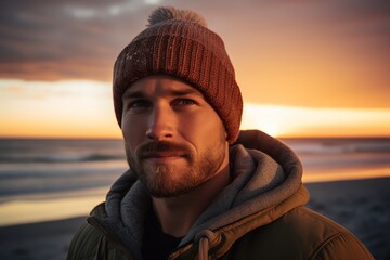 Sticker - Portrait of a tender man in his 30s donning a warm wool beanie in front of vibrant beach sunset background