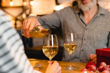 Cropped shot of a happy couple pouring wine into glasses during romantic date for cheering toasting clinking celebration of special event, Christmas, anniversary, engagement, Valentine`s Day