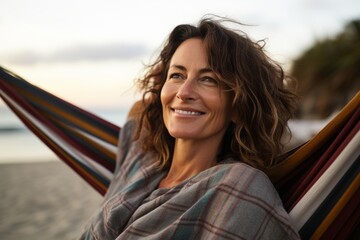 Wall Mural - Portrait of a happy woman in her 40s dressed in a relaxed flannel shirt over relaxing hammock on the beach background