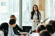 © Jacob Lund - Confident female business owner leading a board meeting, using a laptop to present strategies to diverse team in a modern office setting