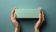 © kiewkoii - Elegant minimalist package held in hands against a soft green background perfect for gift giving or product presentation
