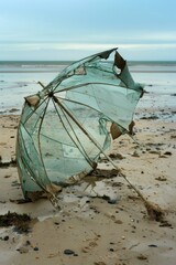 Sticker - A lone umbrella sits on the sand, weathered and worn out