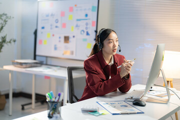 Dedicated businesswoman working late in a dimly lit office, engaged in a video call using a computer and headset for seamless communication