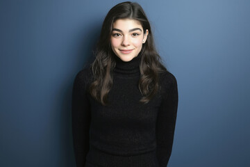 A young woman in a black turtleneck smiles against a blue backdrop indoors