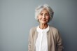 © Markus Schröder - Portrait of a jovial woman in her 70s wearing a chic cardigan while standing against minimalist or empty room background